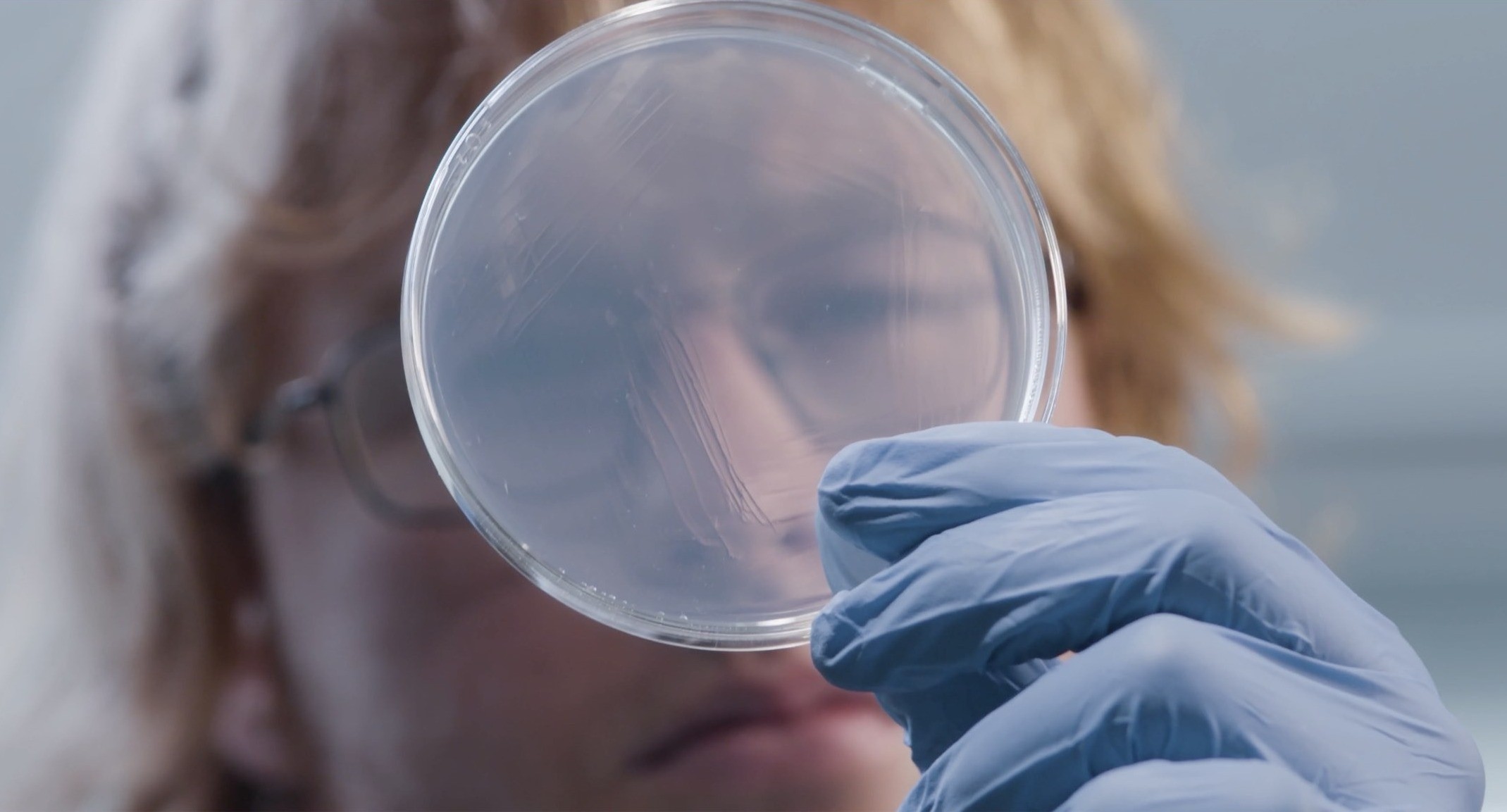 This image shows a female researcher looking through a petri dish .jpg